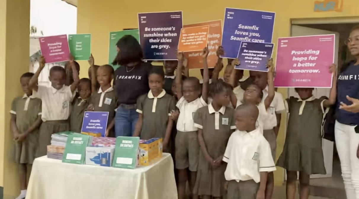 Pupils and Seamfix volunteers holding "Making an Impact" placards at a school outreach